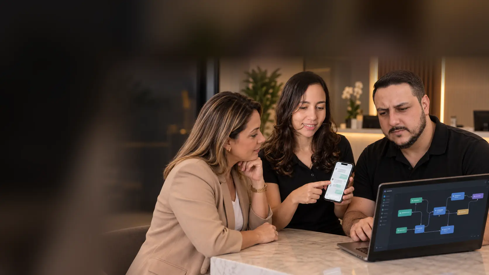 Lari mostrando a uma empresária uma conversa de WhatsApp no celular enquanto o Léo apresenta um fluxo de automação no notebook