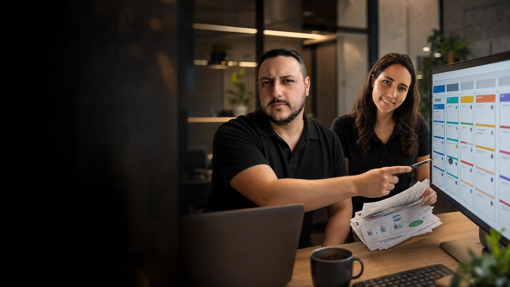 Léo mostrando um funil de vendas organizado em cartões coloridos no monitor enquanto a Lari segura um maço de relatórios impressos