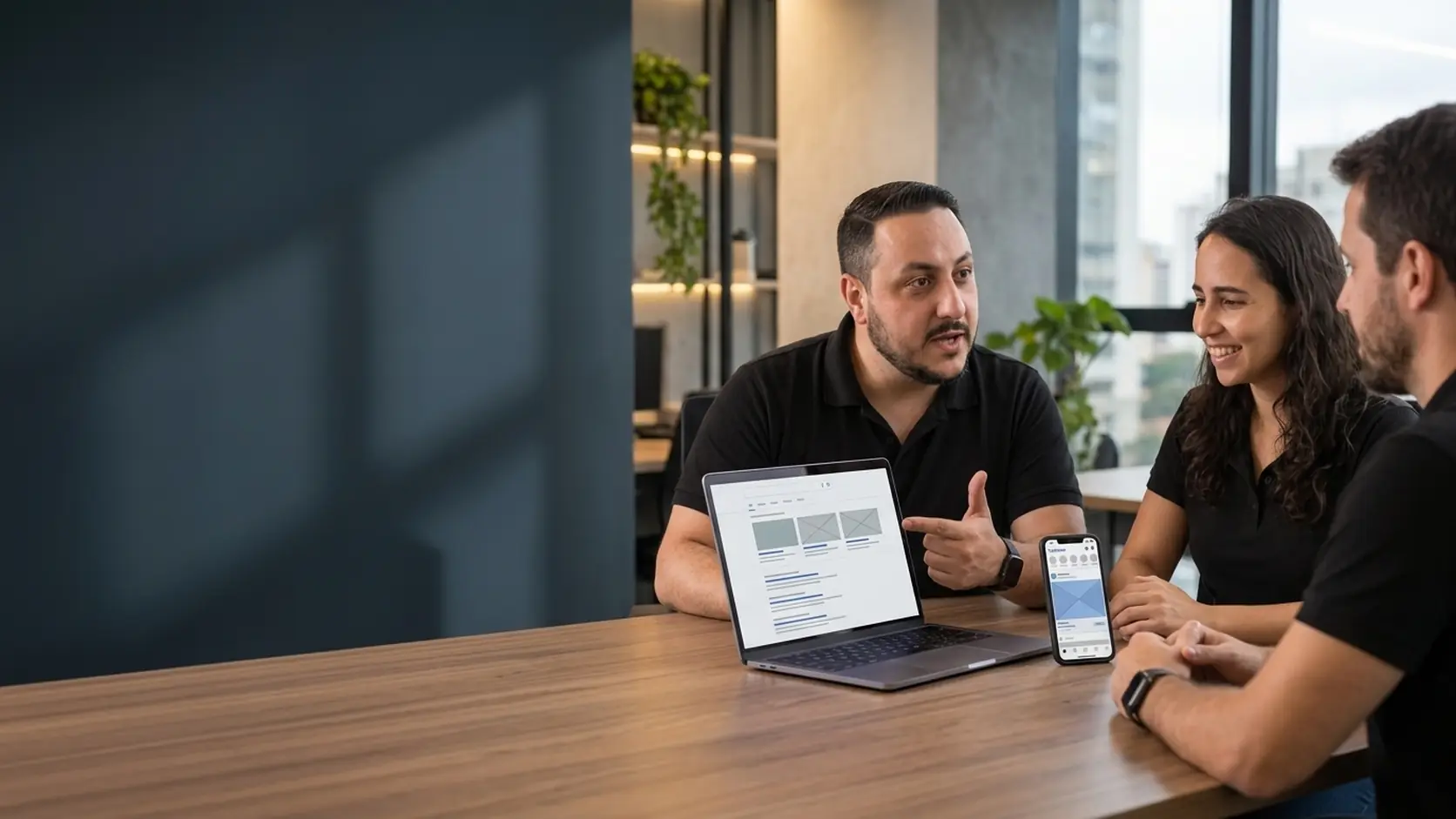 Léo explicando a diferença entre anúncios de busca e de redes sociais com notebook e celular para a Lari e um cliente
