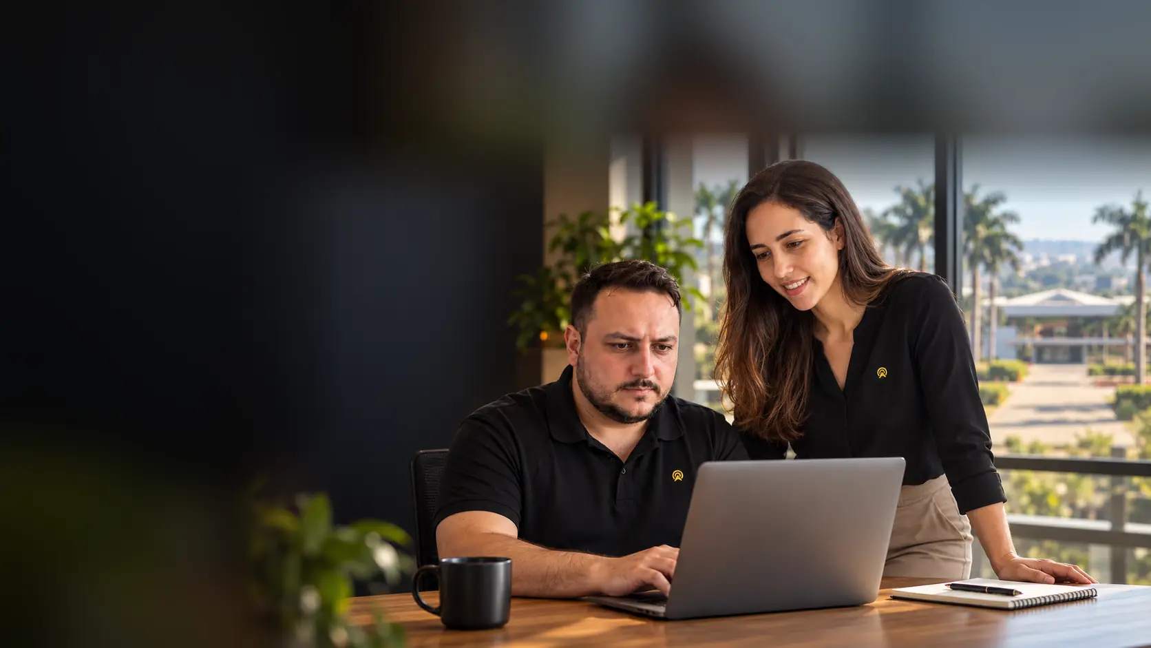Léo e Lari, da Arnoldi Digital, analisando resultados de busca num notebook, com o templo do UNASP de Engenheiro Coelho desfocado ao fundo pela janela