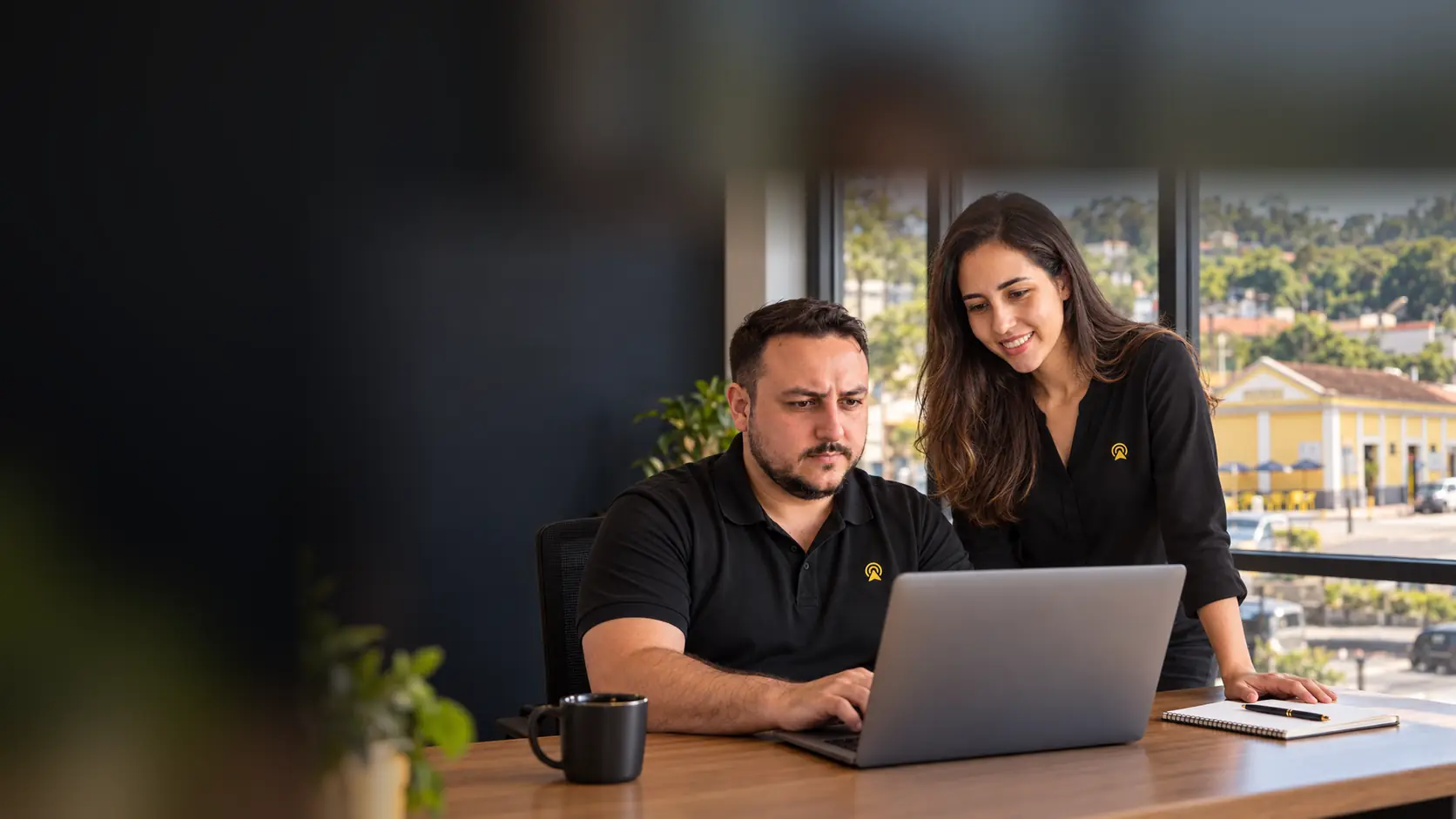 Léo e Lari, da Arnoldi Digital, analisando resultados de busca num notebook, com a antiga estação ferroviária de Pedreira desfocado ao fundo pela janela