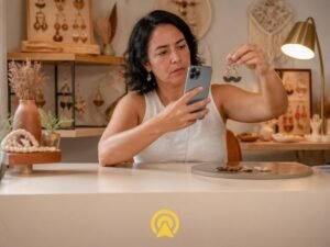 Dona de loja de artesanato fotografando um brinco com o celular para enviar direto numa conversa de WhatsApp