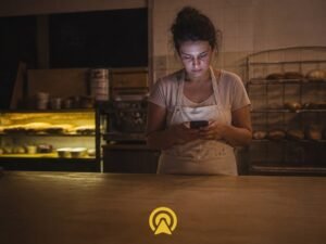 Dona de padaria cansada checando o celular de madrugada, representando mensagens acumuladas fora do horario comercial