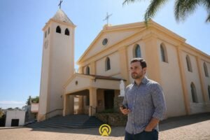 Empresário filmando conteúdo com celular em frente à Igreja Matriz Imaculada Conceição em Morungaba